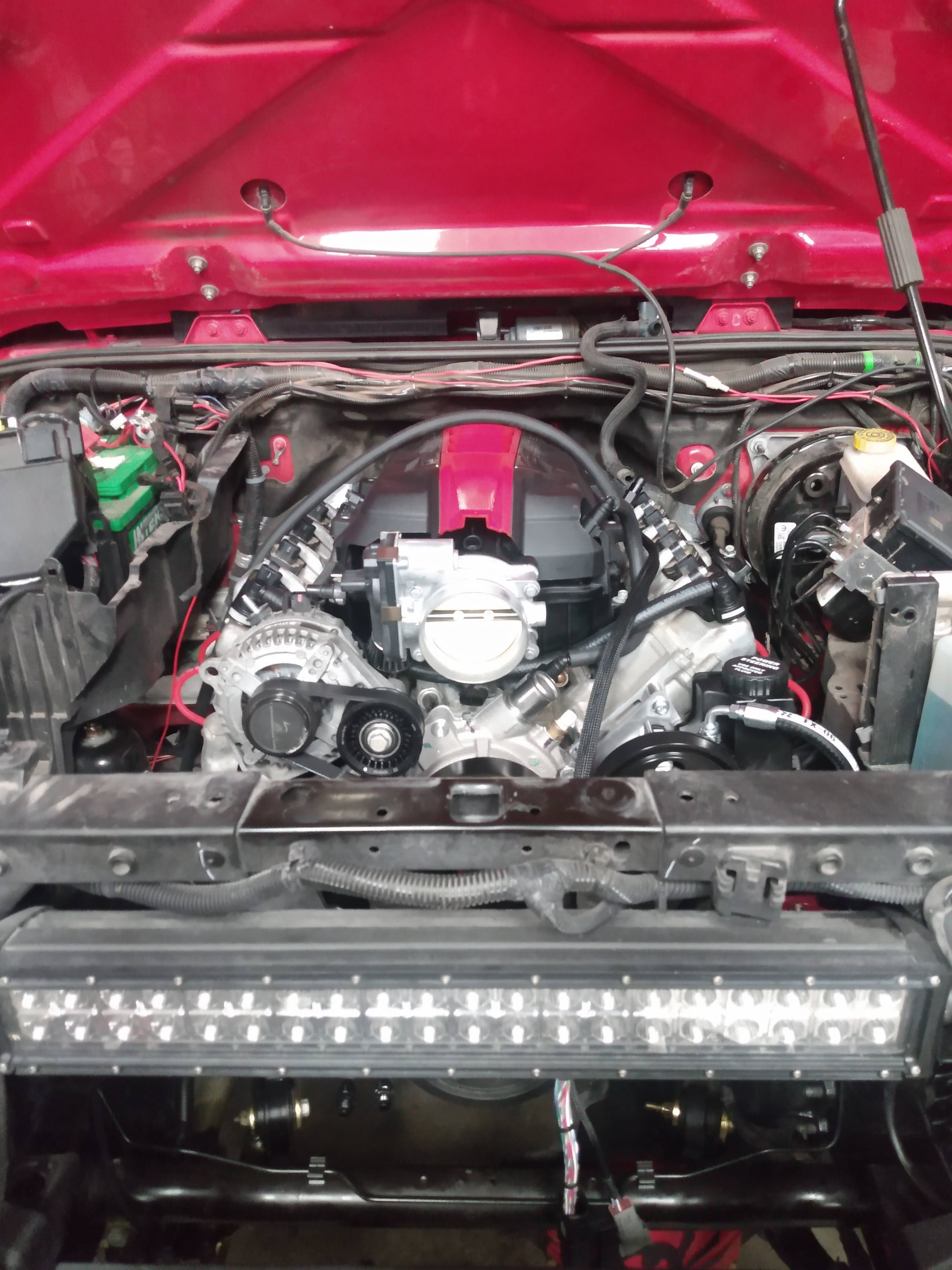 Close-up of Gen V LT V8 engine swap in red Jeep Wrangler JK engine bay showing Wicked Wrench integration harness, ECM mounting, and wiring routing
