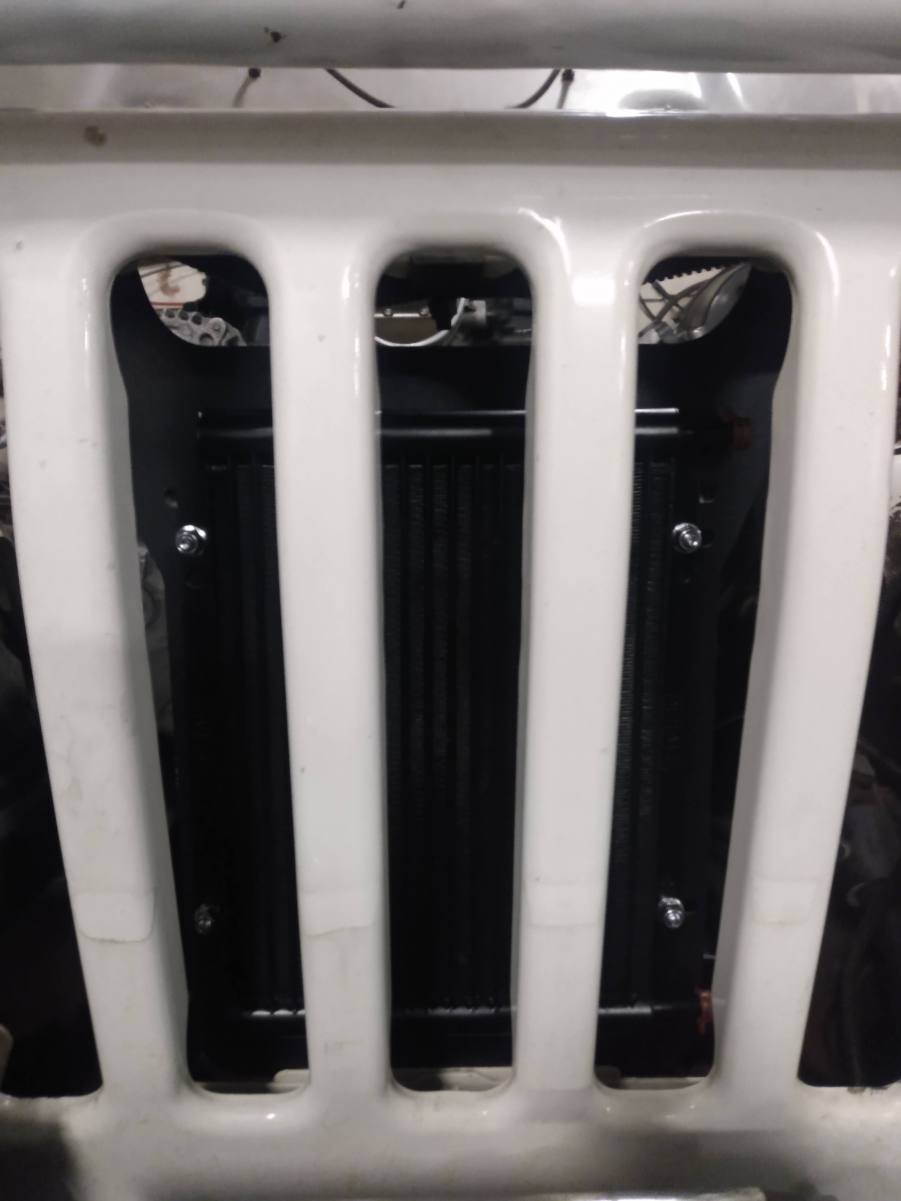 Wicked Wrench Motorsports power steering cooler bracket front view looking through the grille of a Jeep Wrangler TJ or LJ